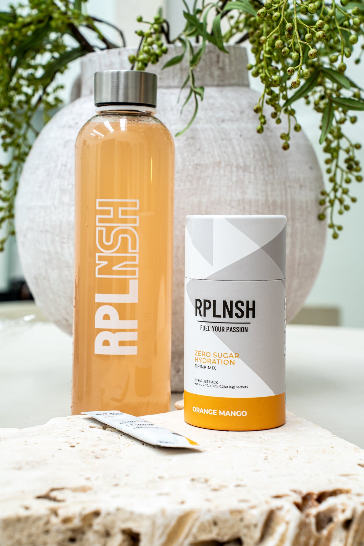 A glass RPLNSH bottle and an Orange Mango pack on a stone block