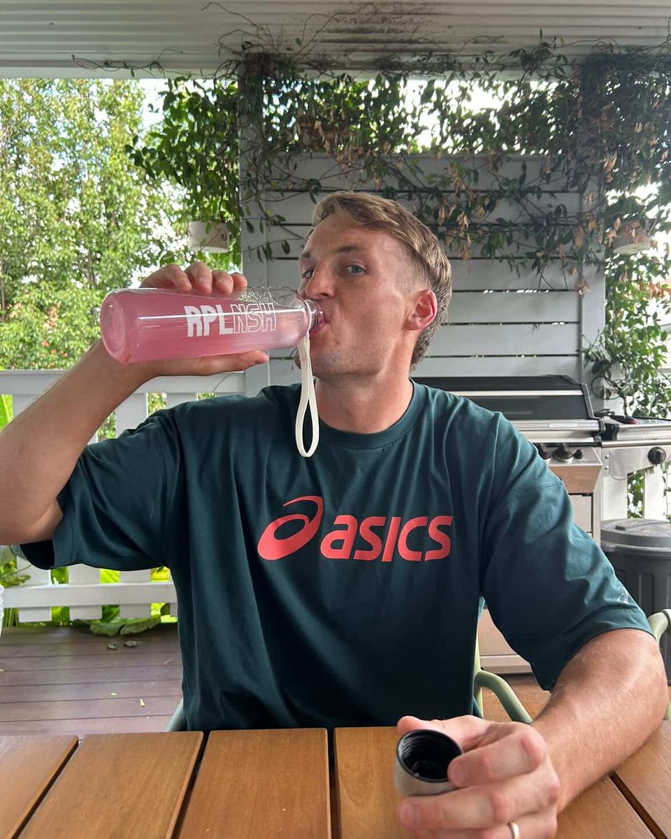 A man drinking from an RPLNSH bottle at an outdoor table