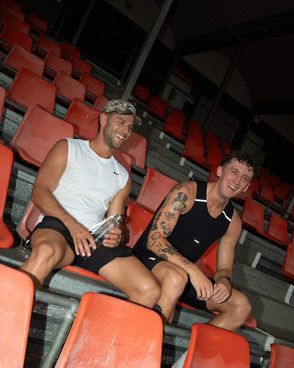 Two men laughing in stadium seats, RPLNSH bottles in hand