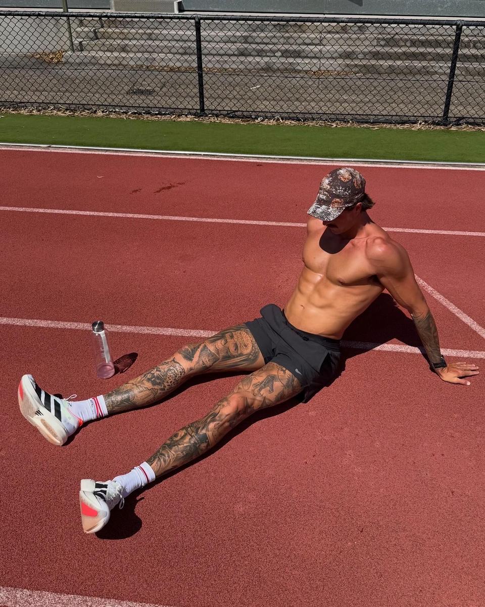 A man resting on a running track, an RPLNSH bottle beside him