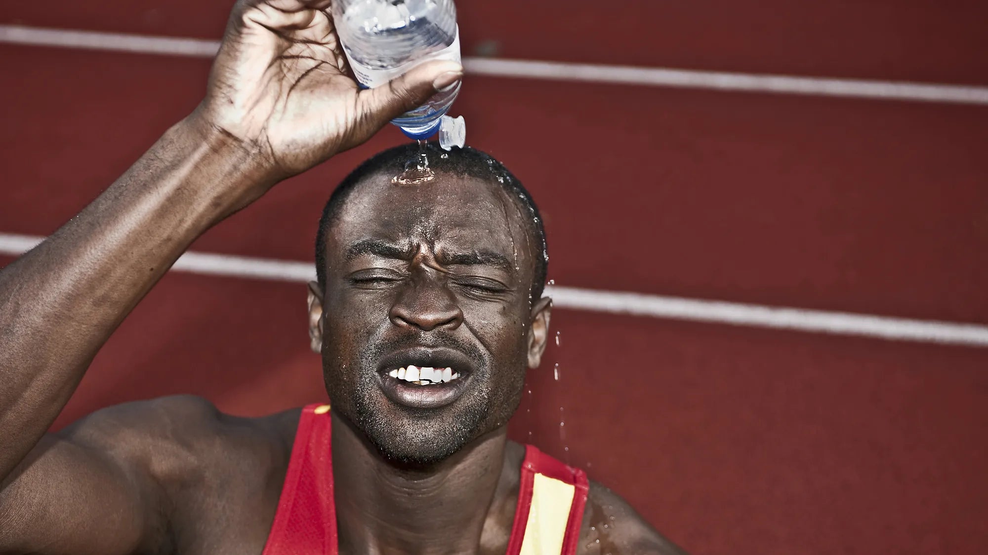 An athlete pouring water over his head on a running track